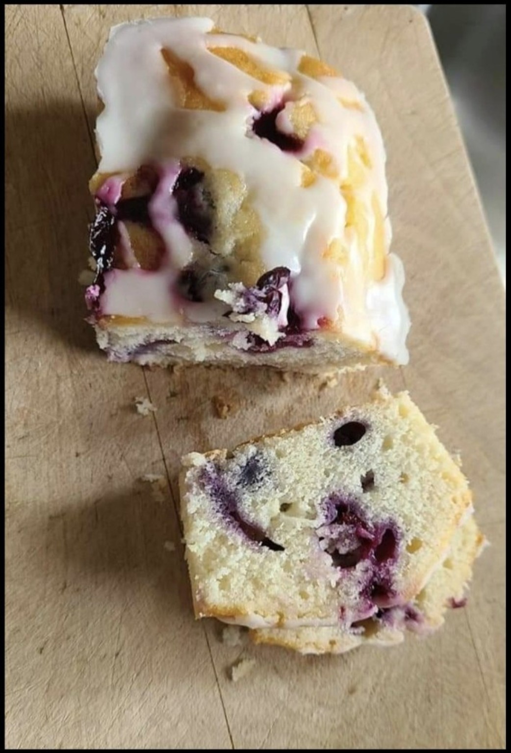 A glazed lemon blueberry mini loaf and a slice on a wooden board